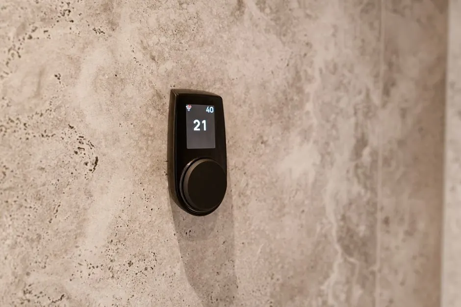 Close-up of a modern sauna temperature control device mounted on a textured stone wall, displaying a digital readout.